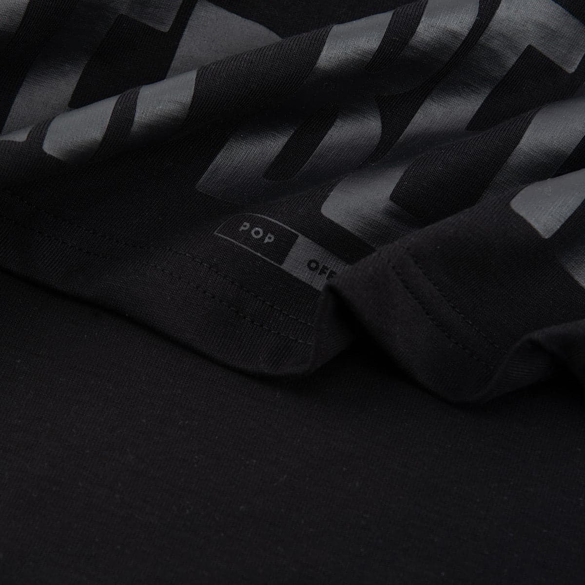 Close-up of the tonal BETTER BELIEVE IT lettering at the hem and the woven Popoff tab