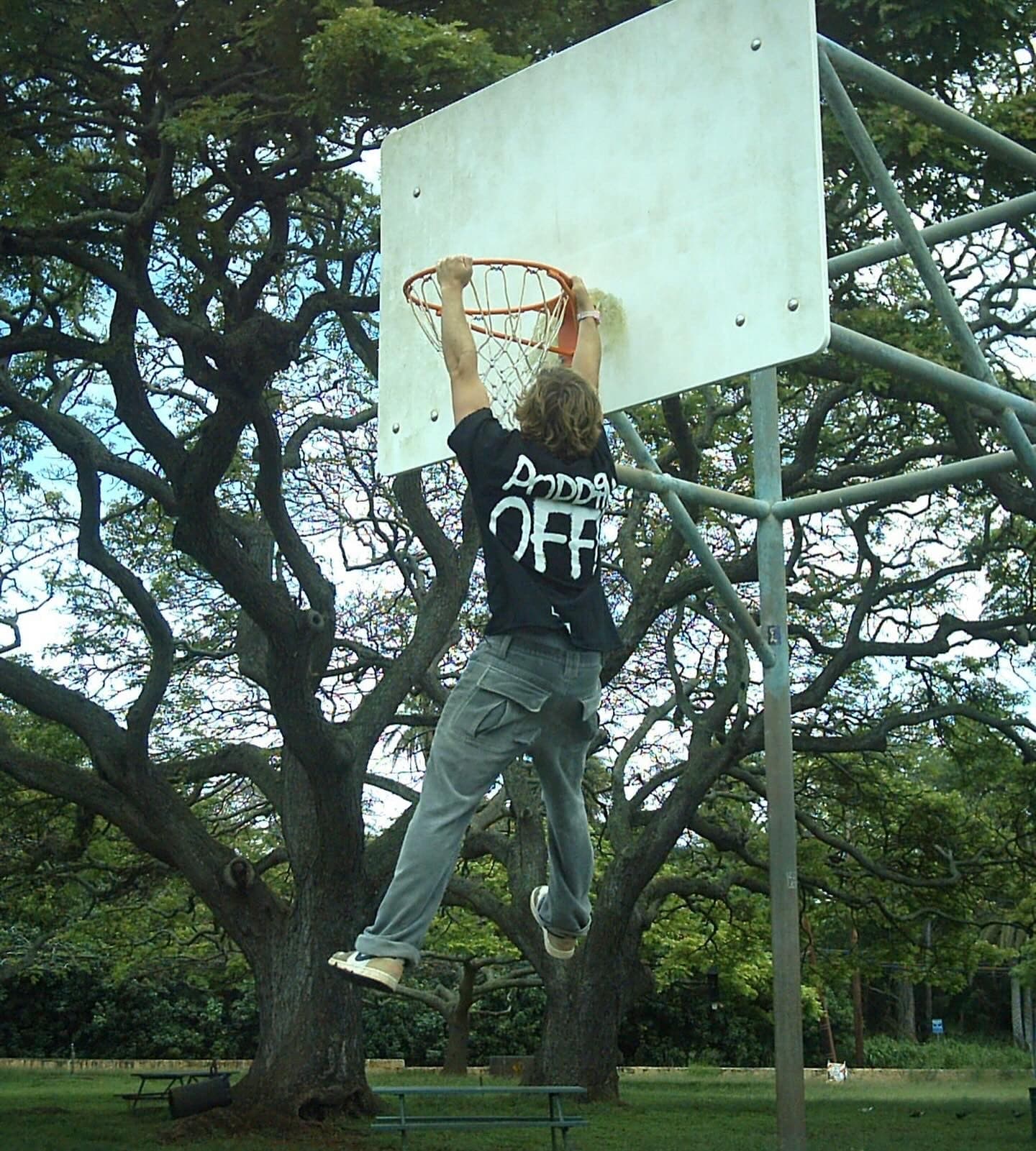 Someone hanging from a basketball hoop in the black Poppin Off tee, back print showing