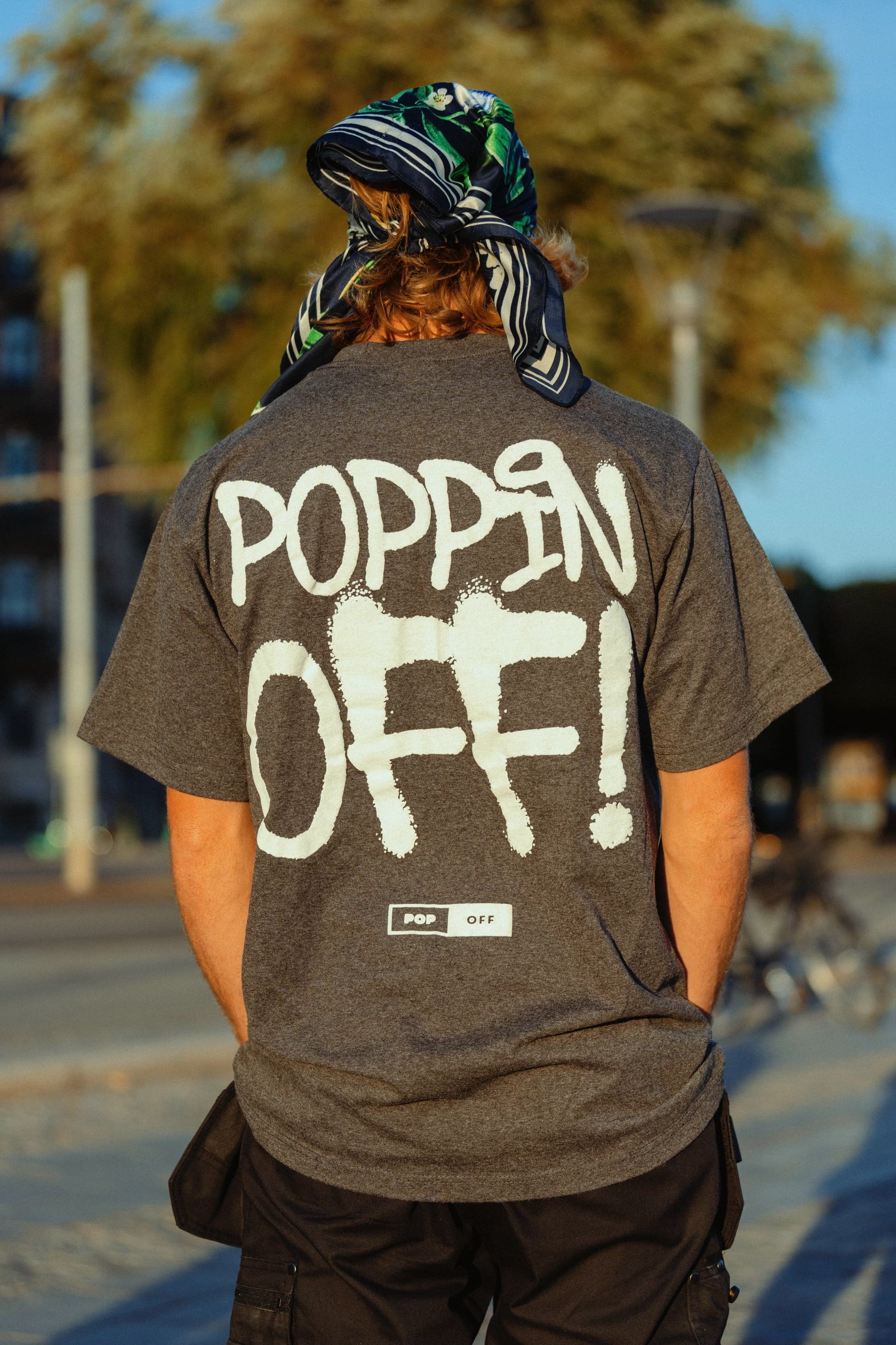 Back view of someone in a bandana wearing the grey Poppin Off tee on a waterfront