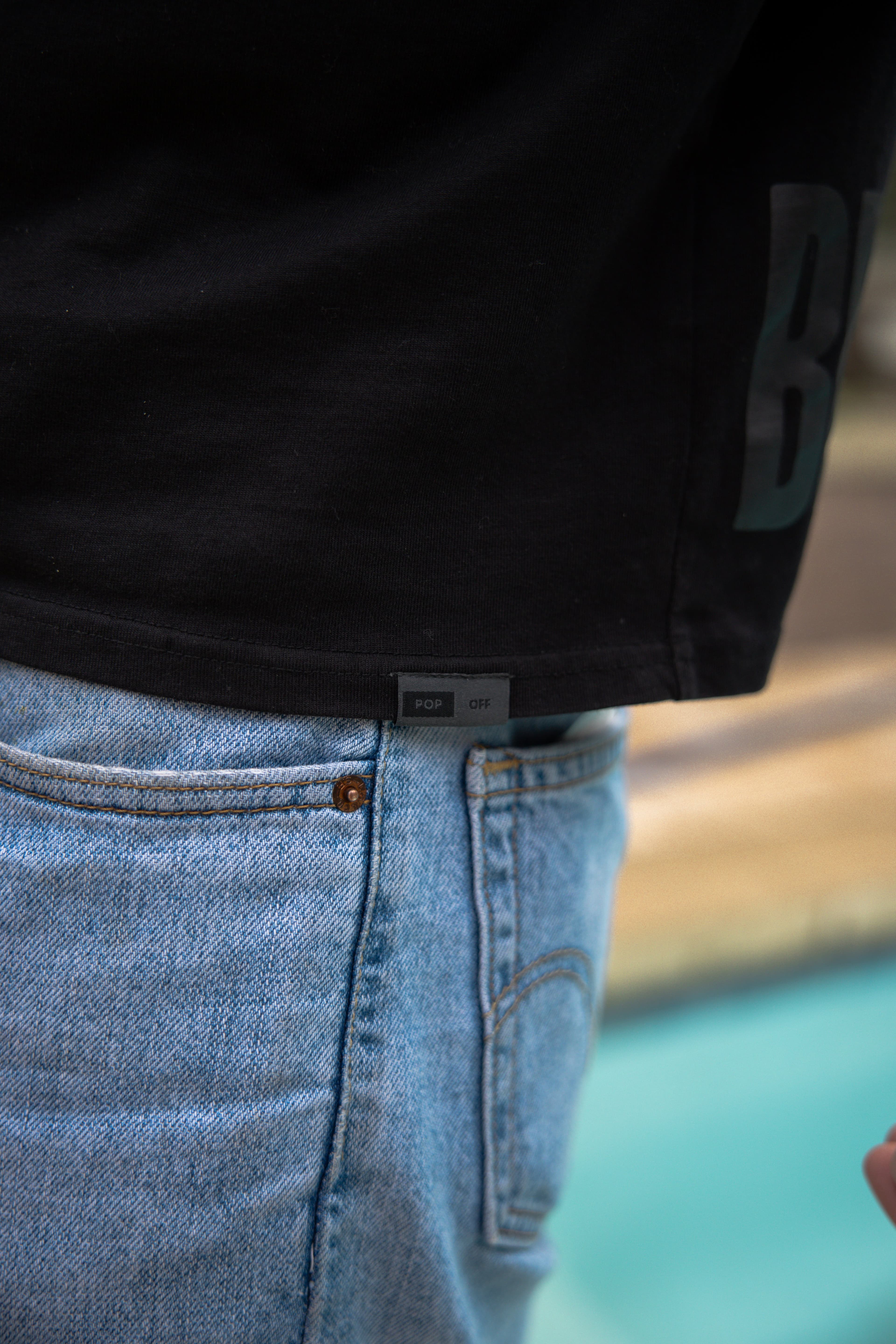 The cropped hem of the black tee over light jeans, by a pool