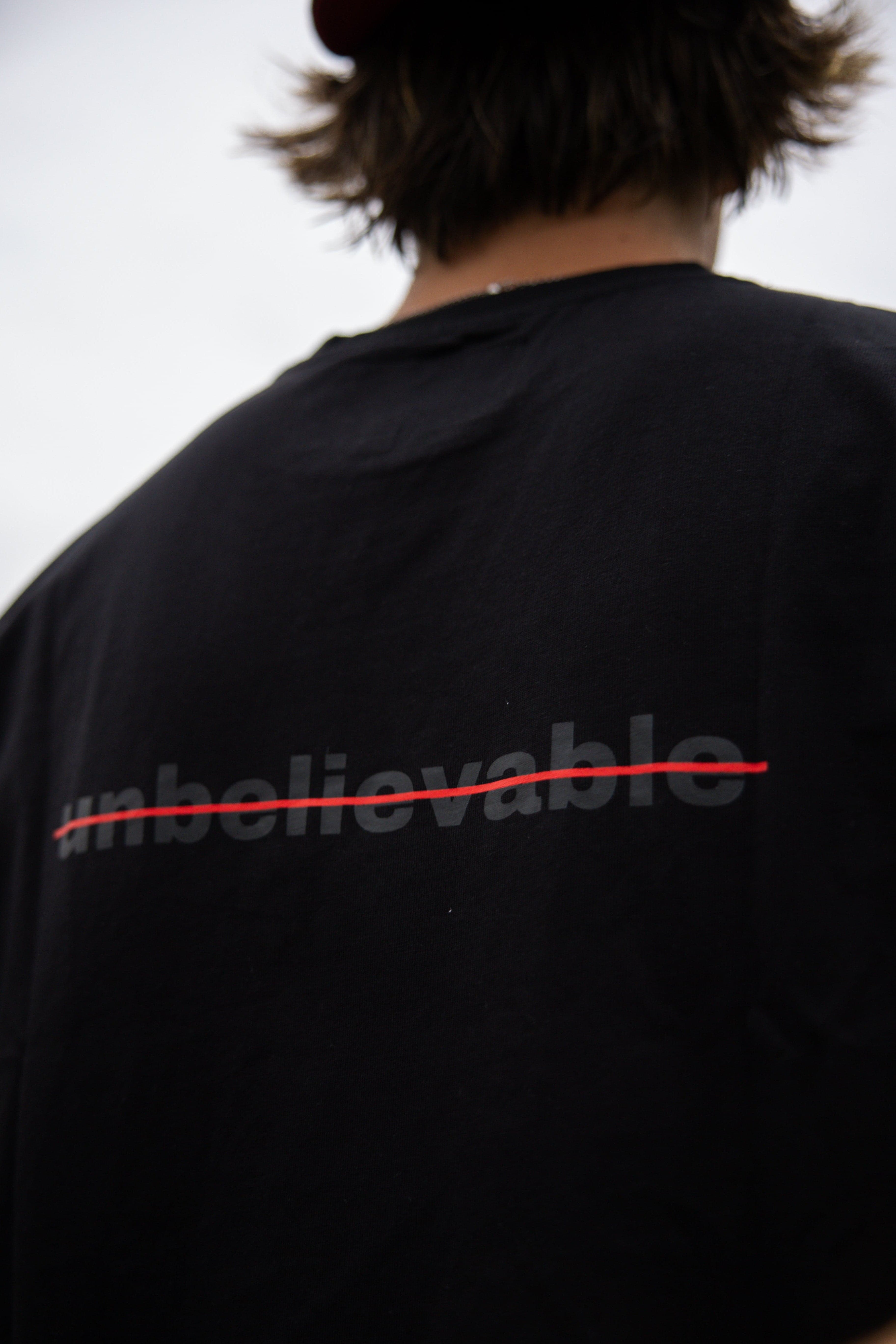 Back of someone in the Better Believe It tee, “unbelievable” crossed out in red