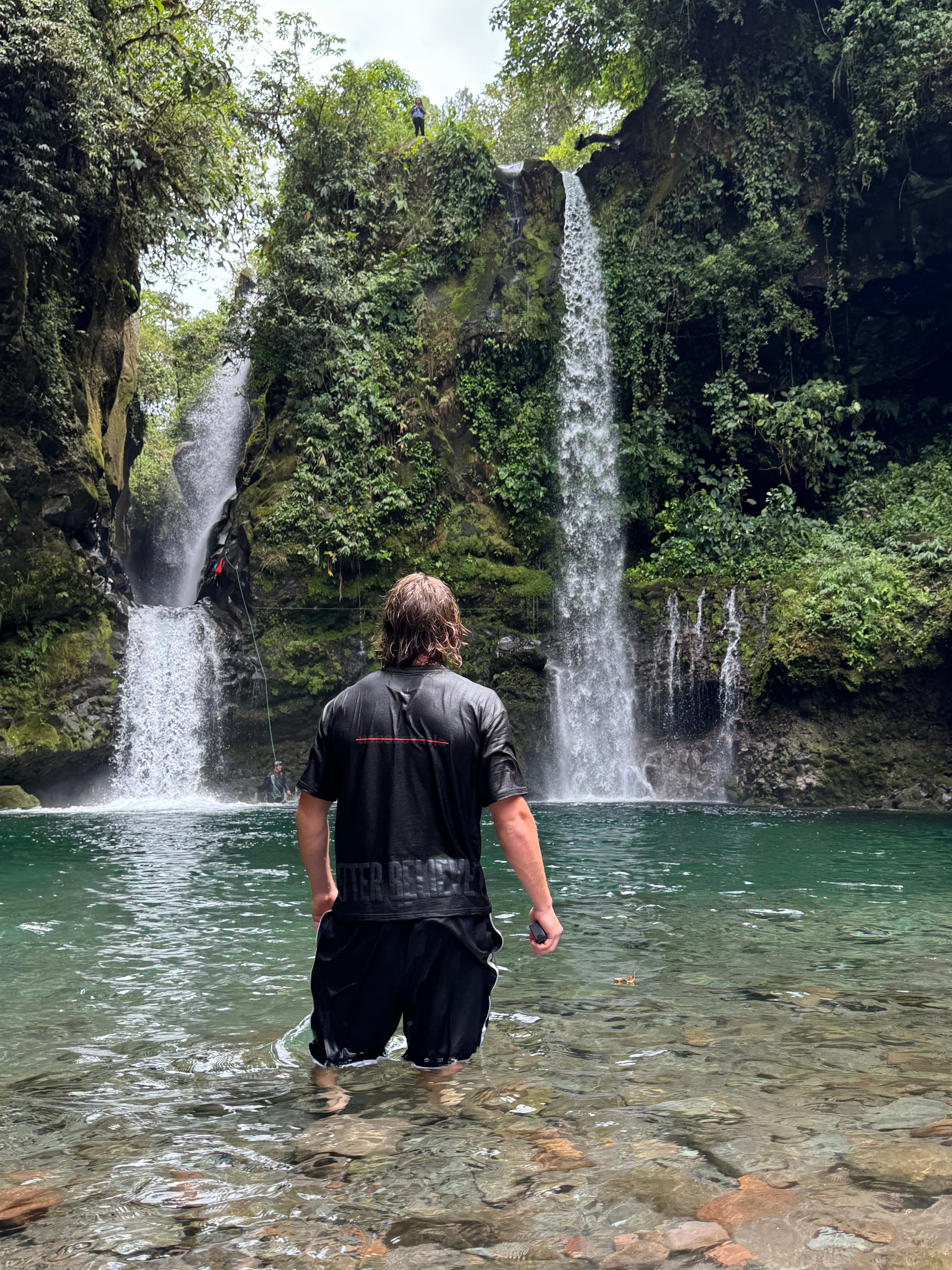 Someone wading toward twin waterfalls in the Better Believe It tee