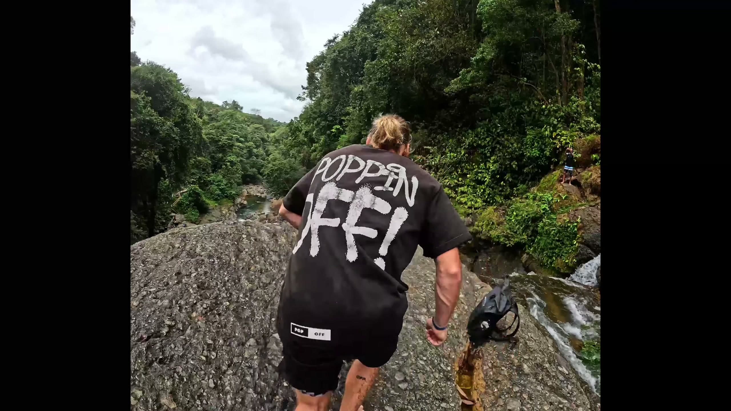 A Popoff Adventures crew member hiking a riverbed in a black Poppin' Off shirt
